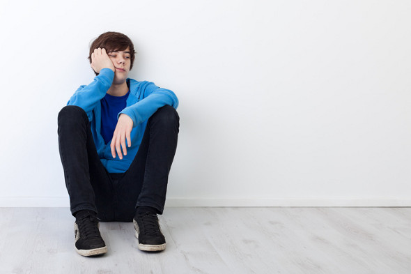 I am not in the mood today - bored teenager boy sitting by the wall